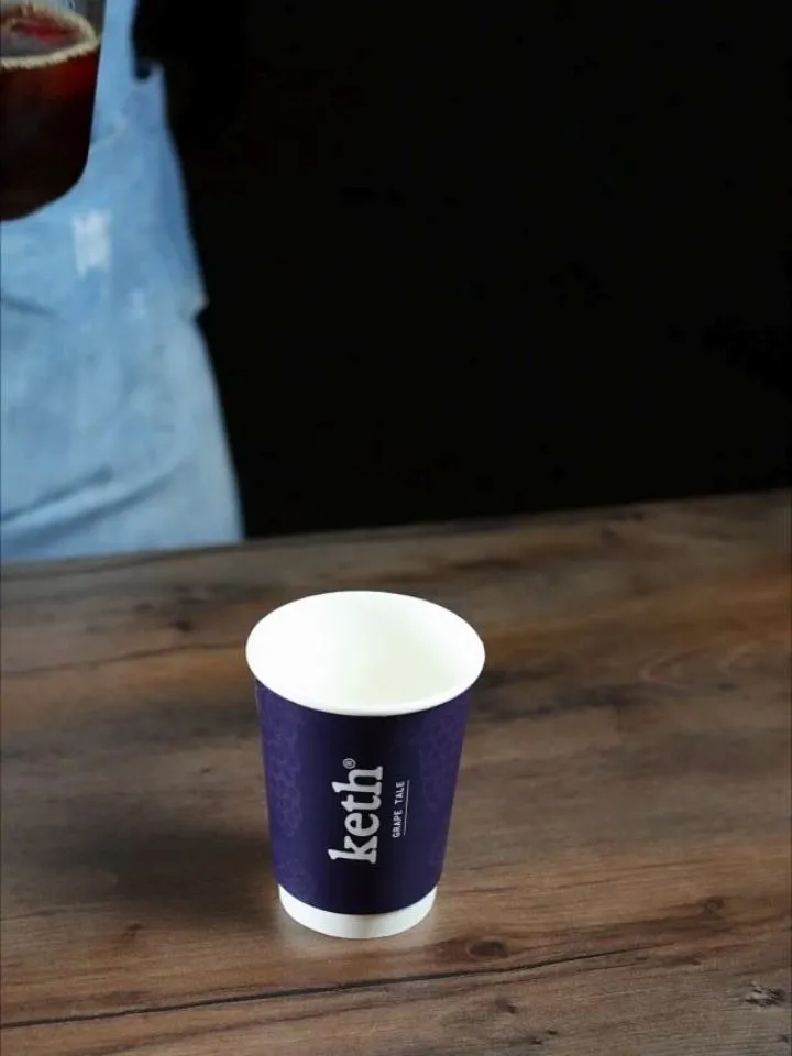 A barista in an apron behind a navy Grape Tale cup on the wooden bar