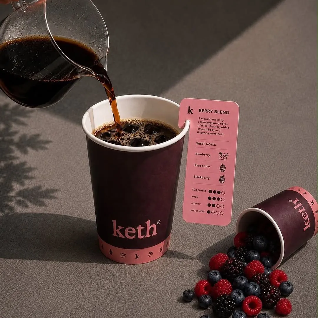 Coffee poured from a glass server into a Keth Berry Blend cup over ice, with fresh berries